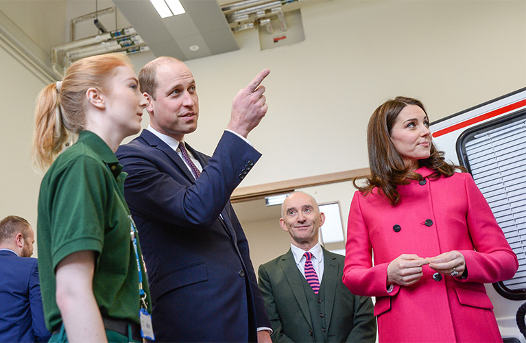 The Duke and Duchess of Cambridge with a paramedic science student looking and pointing to the mock ambulance