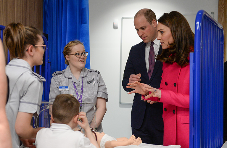 The Duke and Duchess of Cambridge talking to two nursing students who are practicing on a child mannequin