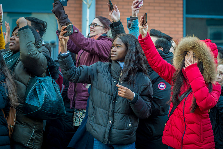 A group of young adults holding phones trying to capture a picture of the Duke and Duchess of Cambridge