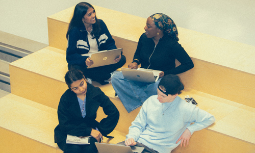 Four students sat working together on a large yellow stepped seating area