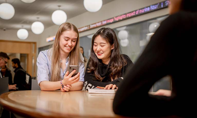 Two female students looking at a smartphone together and smiling.