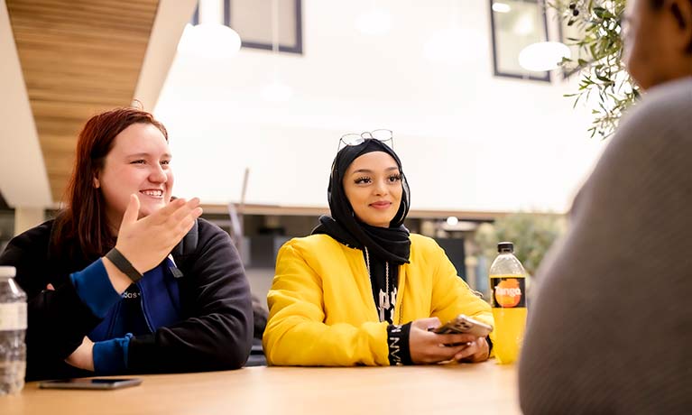 Two females chatting across a table in the Coventry Uni hub 