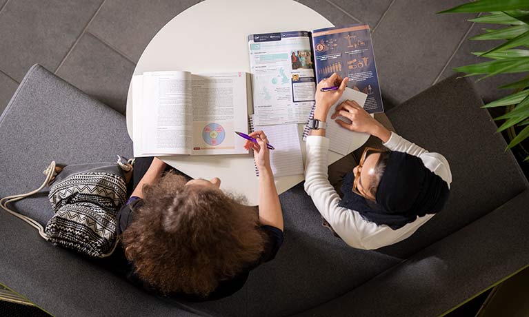 Aerial view of two students looking at textbooks in a breakout area