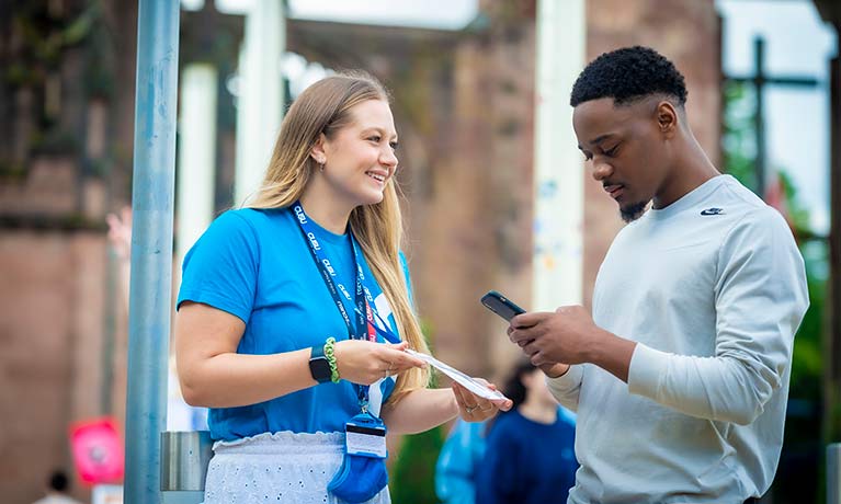 Student support officer showing a prospective student a leaflet. Student is holding a phone. 