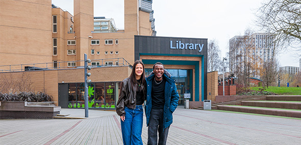 Two students stood smiling in front of the library