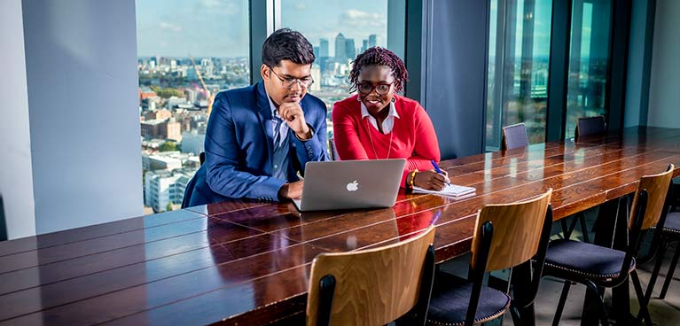 Professional man and lady at a board table looking at a laptop