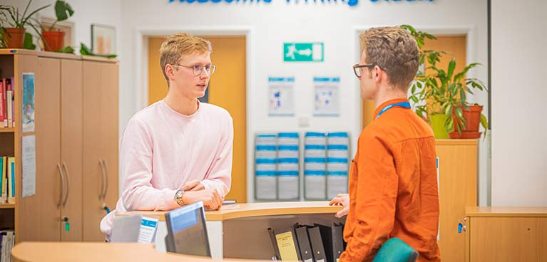 student standing at a reception desk speaking to someone behind the desk