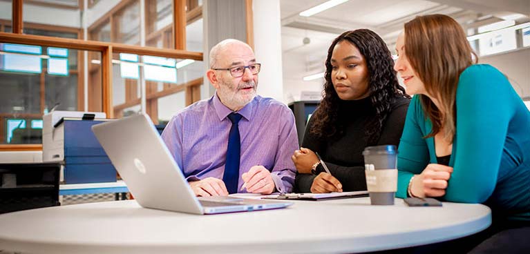 Two women and man sat at table looking at a laptop
