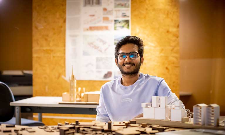 An architecture design at a table with building designs, smiling at the camera.