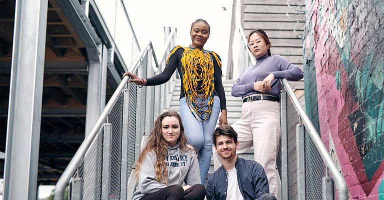 Four students smiling at the camera on outside stairs 