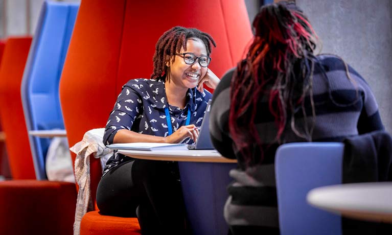 Student smiling sitting in a large orange chair facing another person. 