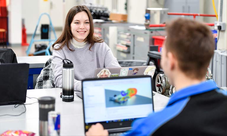 young female student smiling across a table at another student working in a engineering study area 