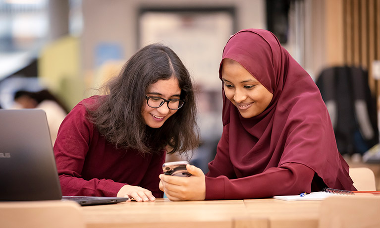 Two students smiling and looking at a mobile phone.