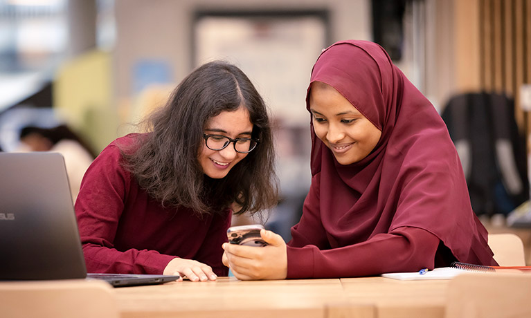 Two women smiling and looking at a mobile phone.