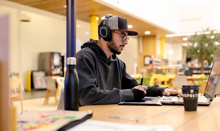 Student wearing headphones looking at a laptop in bright student hub 