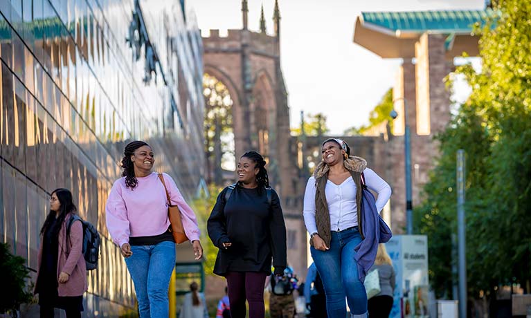 Three ladies walking and smiling alongside Coventry Cathedral ruins 