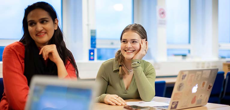 Two female students sat with their laptops smiling