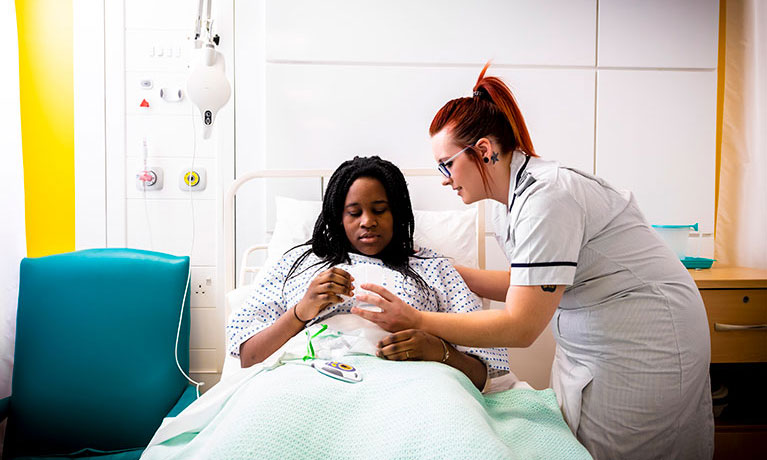 Student nursing caring for a patient in a hospital bed