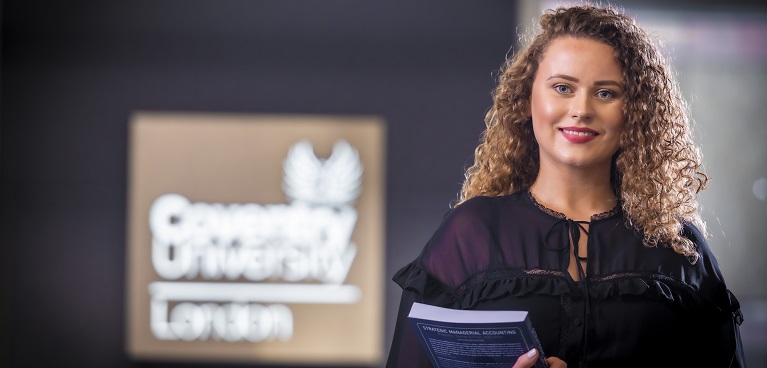 A student smiling at the camera holding a textbook