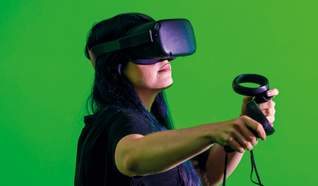 A student wearing a VR headset in front of the green screen in The Tank studio.