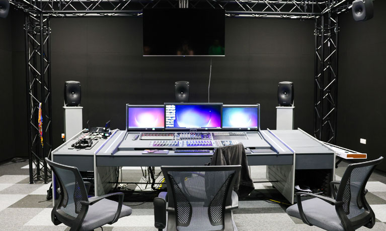 Immersive sound studio with equipment for audio production on a large desk with chairs and speakers around the room