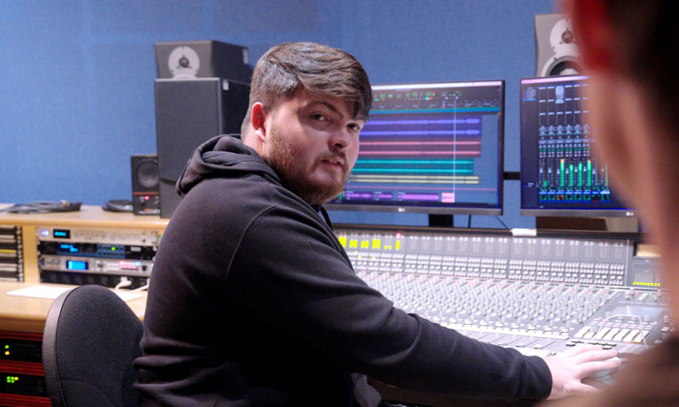 A student sat at the control panel in the recording studio