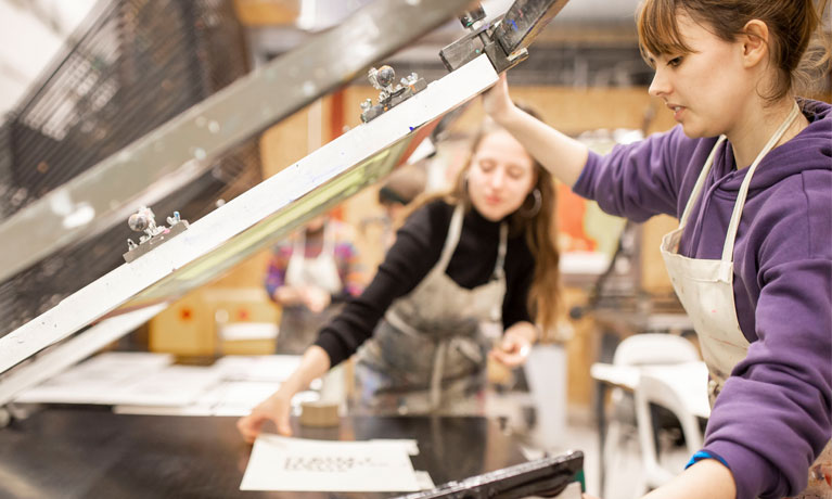 Students using a screen printer in the print workshop