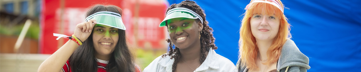 Three students sat outside during Coventry University's welcome week, wearing colourful visors.