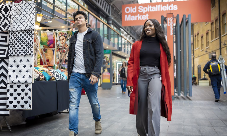 Two Coventry University London students walking through the bright and diverse Spitalfields indoor market.