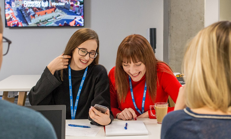 Students working in a group, smiling while looking at a smartphone.