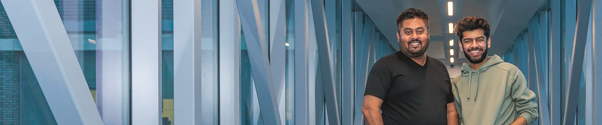 Two male students walking through a glass walkway smiling