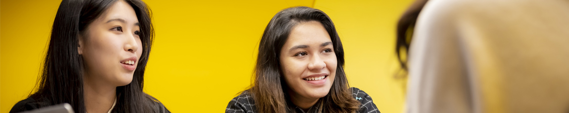 international students smiling while sat around a table against a yellow background