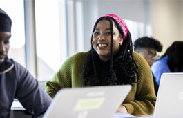 International student smiling in a classroom while others around her work on laptops