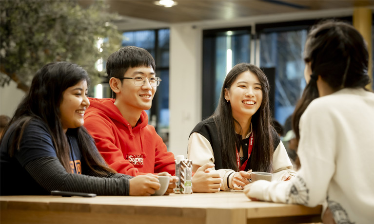 international students sitting chatting around a cafe table in the Hub.