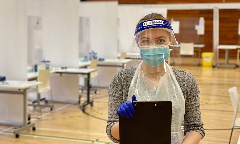 Biomedical Science student Alicja Szkolnik wearing a face shield and PPE apron holding a clipboard
