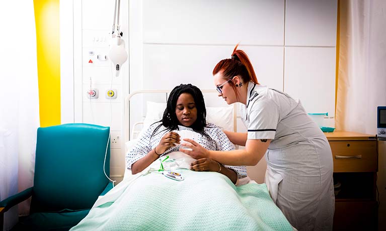 trainee nurse caring for a female patient sitting up in bed 