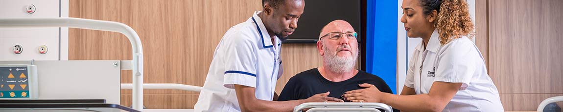 Two nurses helping a male patient on a frame.