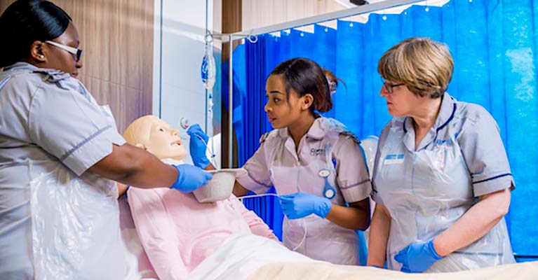 Student nurses inserting tube into dummy's nose