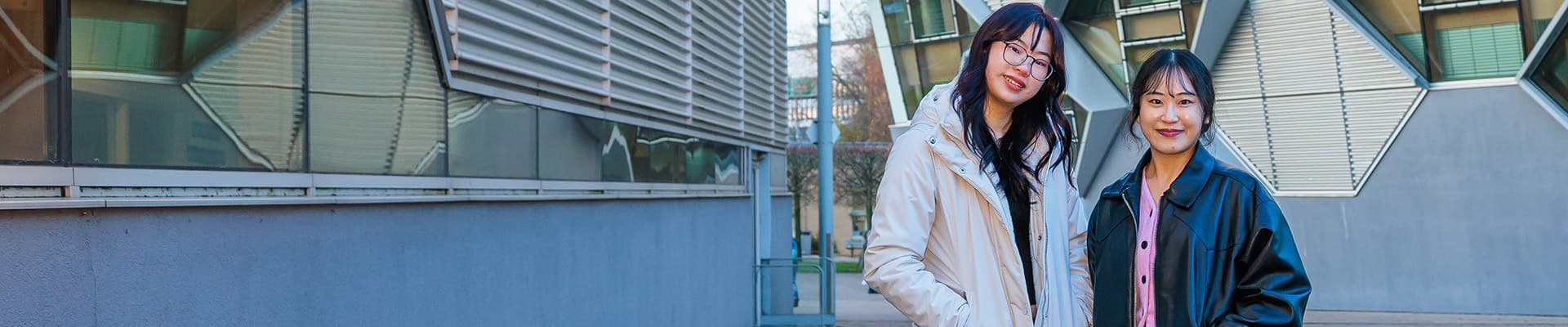 Two female students stood together smiling outside of a building