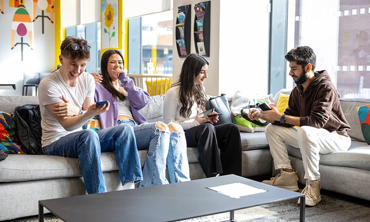 Group of students sat in a communal area laughing and looking at their phones