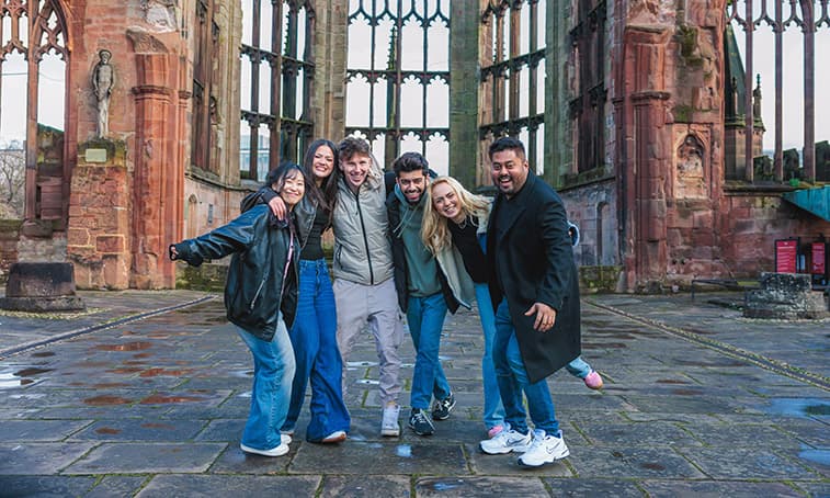 Group of students stood smiling in the cathedral ruins
