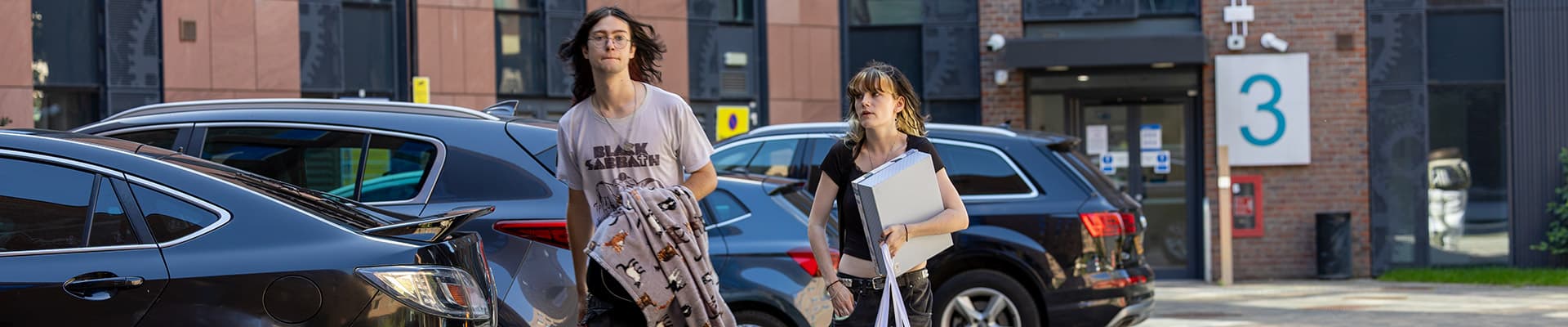 Two students walking to Godiva Place with bags and boxes