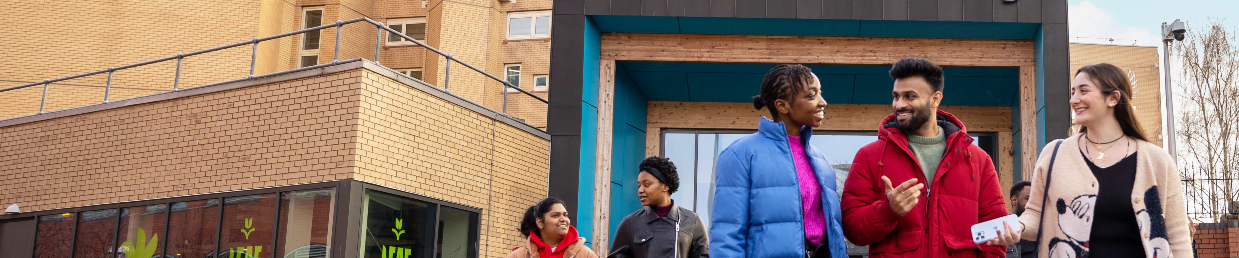 Group of students walking and chatting outside the Coventry University library