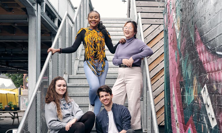 Four students sat on steps and smiling at the camera in Coventry's Fargo VIllage.