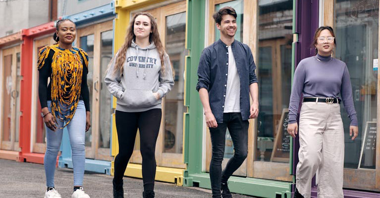 Four students walking through Fargo Village in Coventry, with colourful shops behind them.
