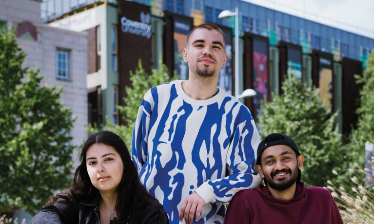 3 students posing outside a campus building with greenery in the background