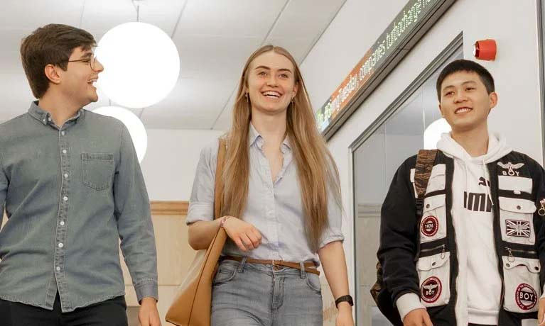 Three students smiling and walking along a corridor
