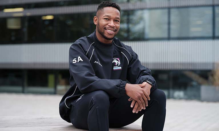 Male postgraduate student sitting and smiling outside