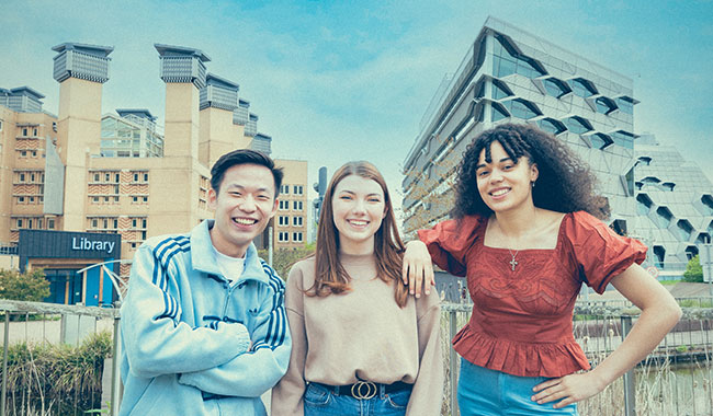 Three students on campus with the Frank Whittle building and the library in the background 