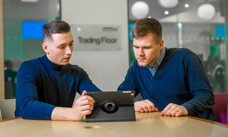 Two students sat at desk looking at iPad.